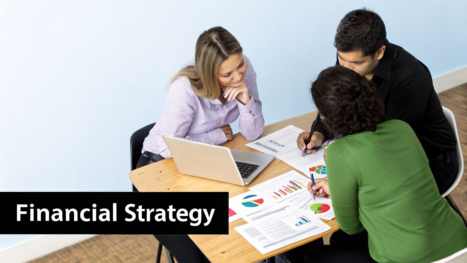 Three professionals analyze financial reports and charts on a table with a laptop, discussing financial strategy.